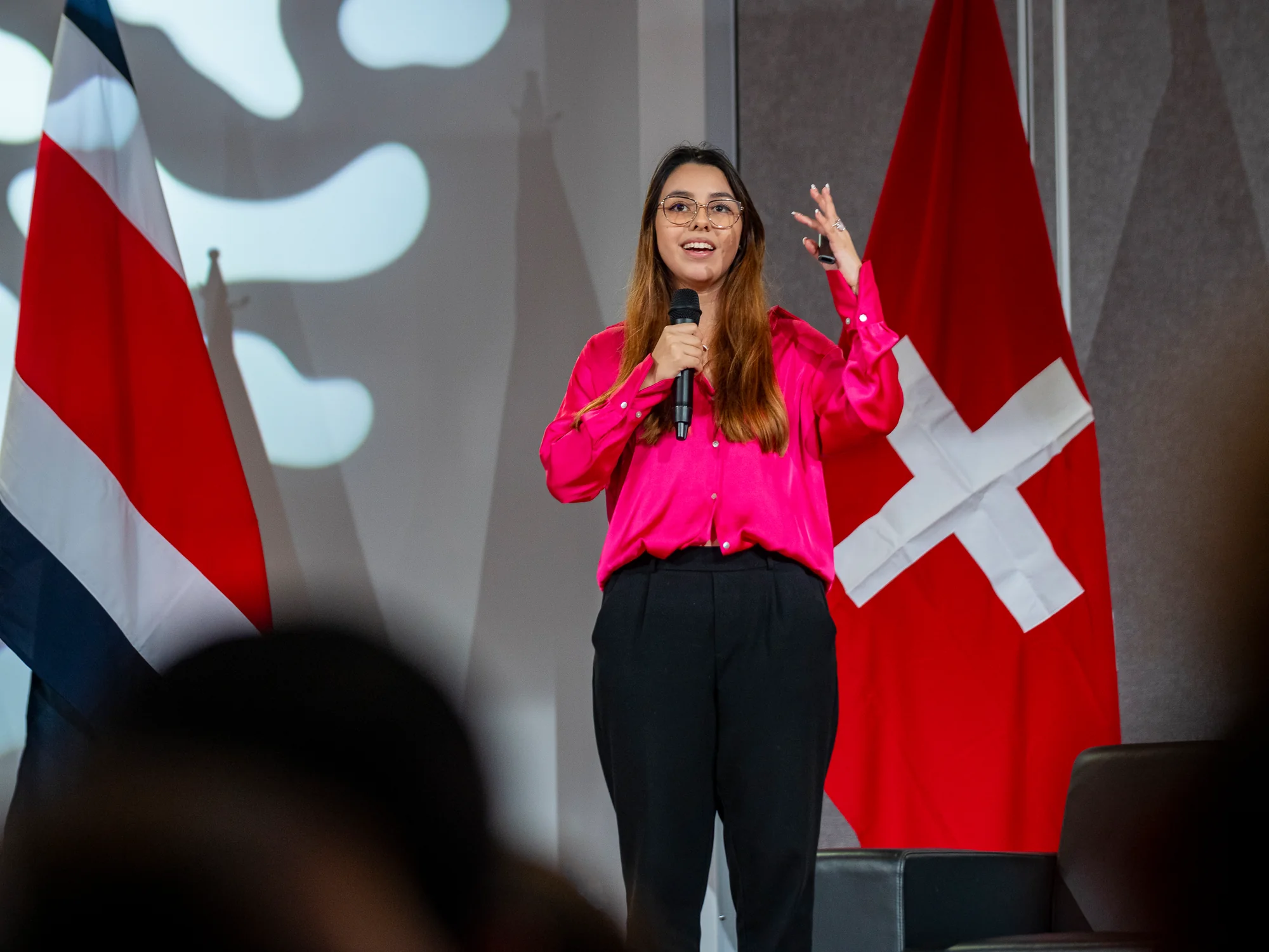 Invitada dando su charla de pie con micrófono, con las banderas de Costa Rica y Suiza de fondo