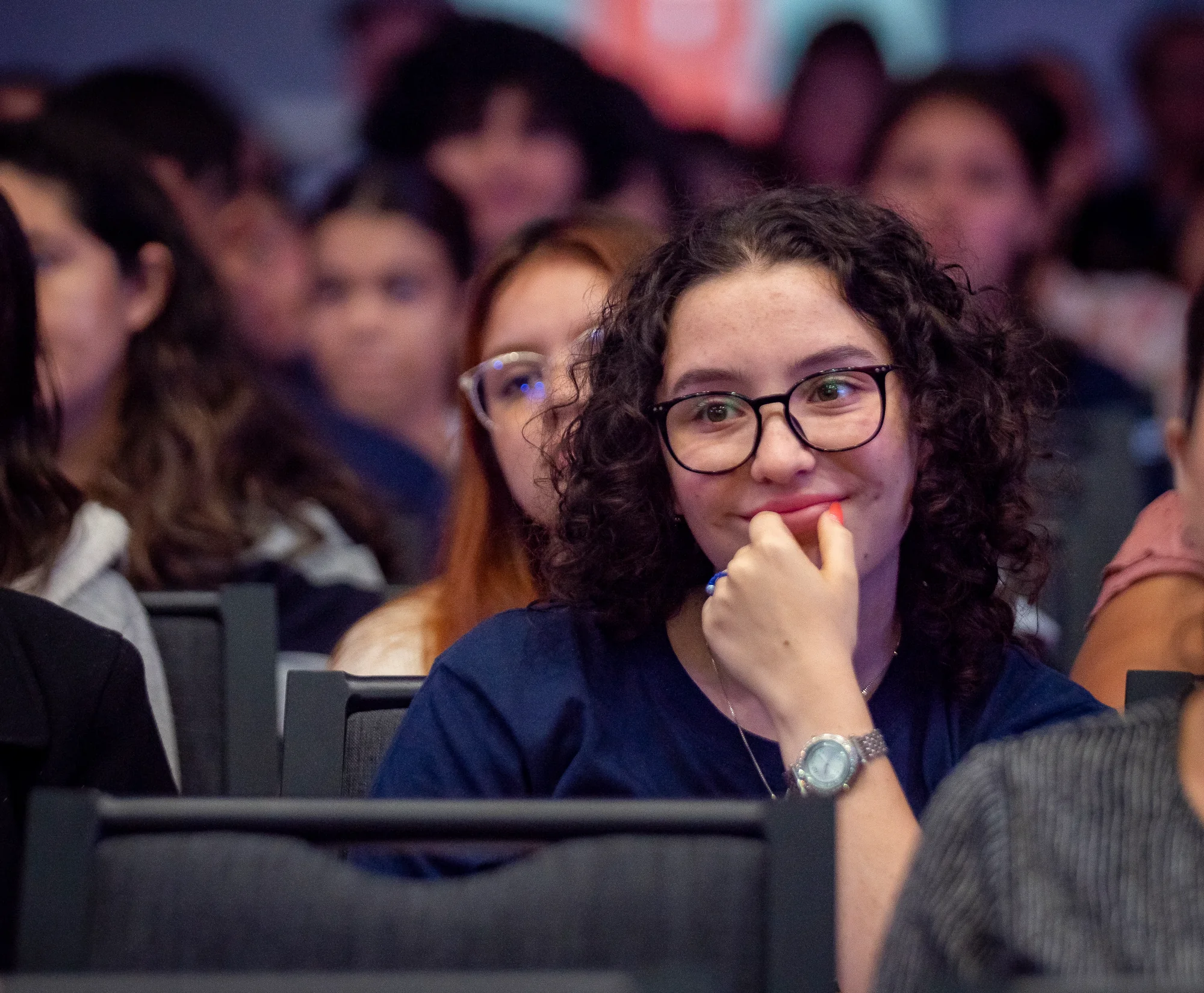 Joven del público escuchando con atención, con anteojos y cabello rizado