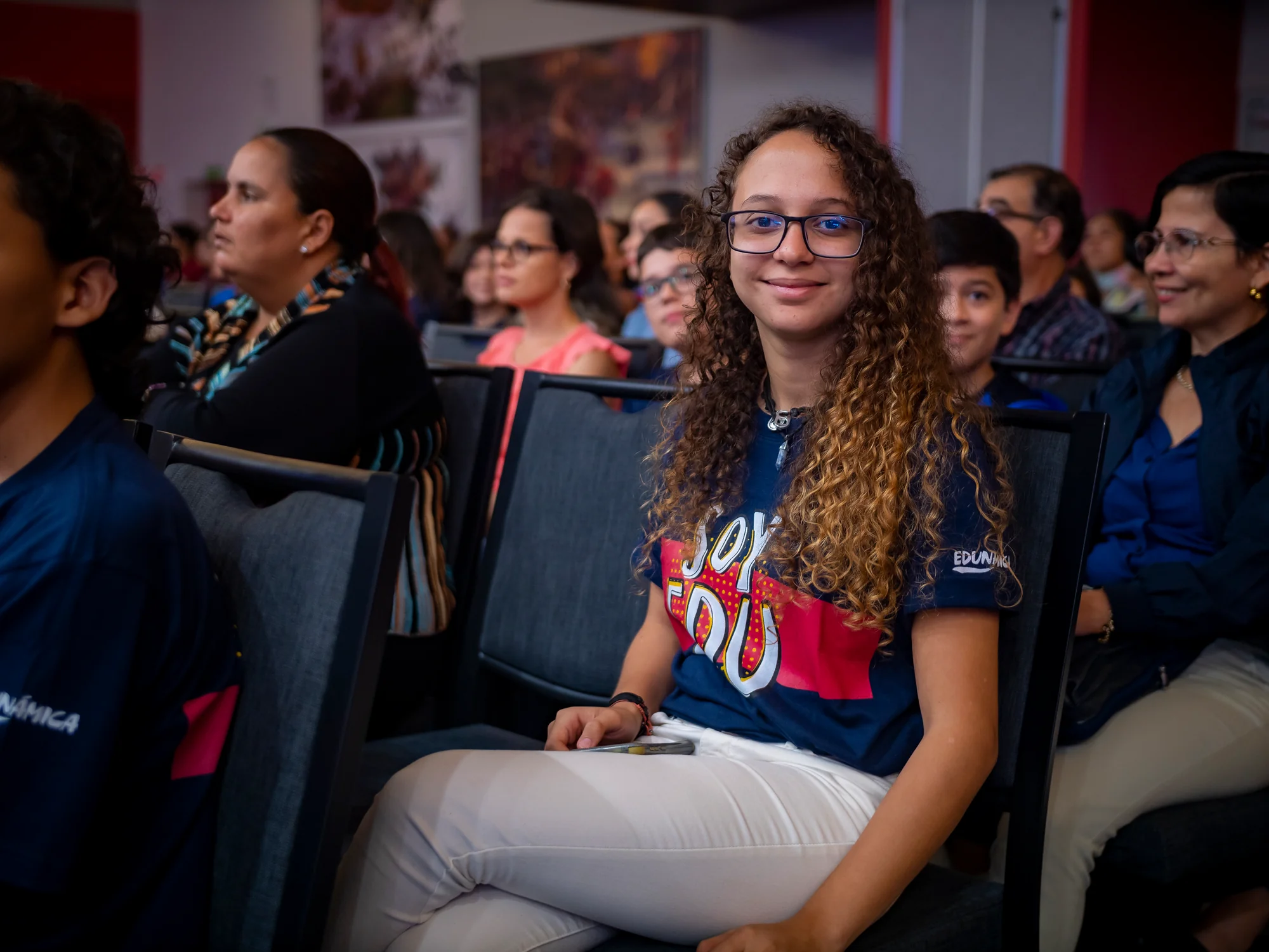 Joven del público con camiseta de Edunámica, sonriendo entre el resto de asistentes