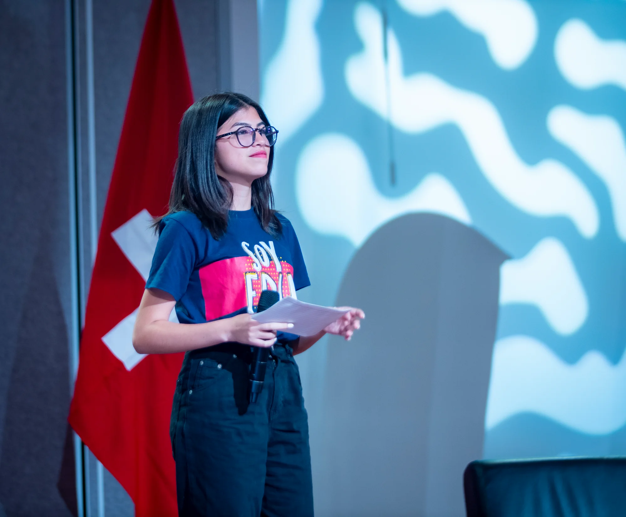 Joven anfitriona de Edunámica presentando con micrófono y guion en mano