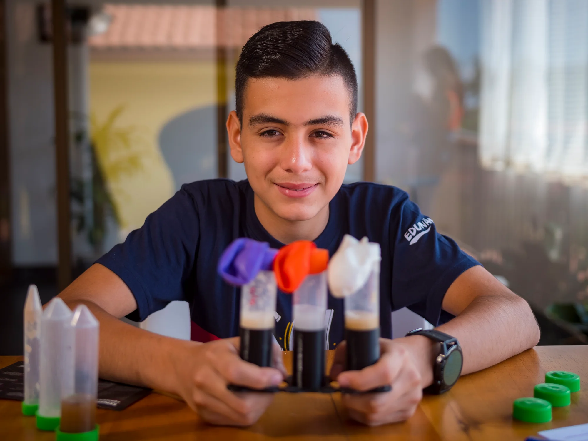 Beneficiario de Edunámica mostrando un experimento científico casero con tubos de ensayo y globos de colores