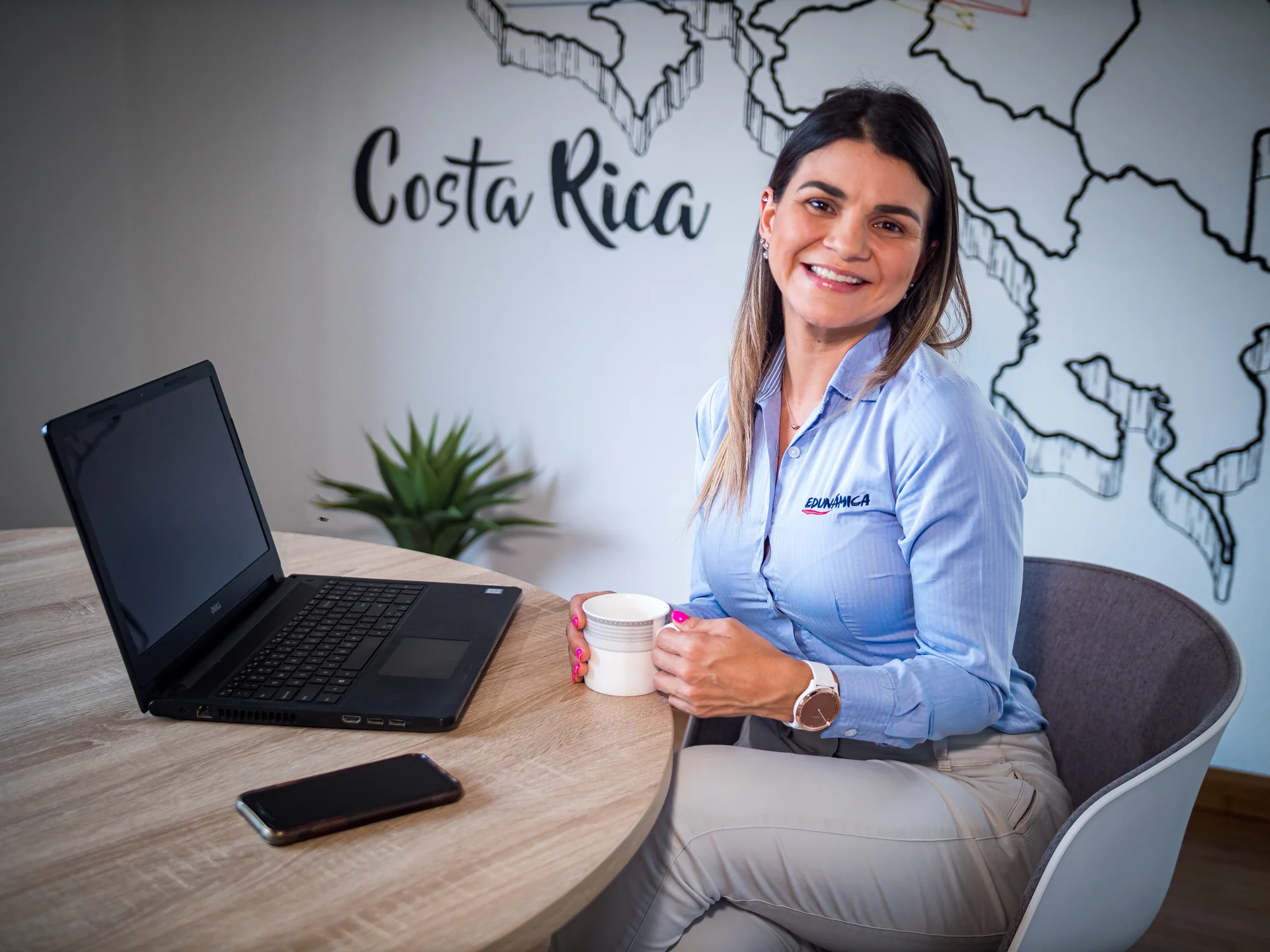 Retrato institucional de una colaboradora de Edunámica con una taza de café, frente a un mural con el mapa de Costa Rica