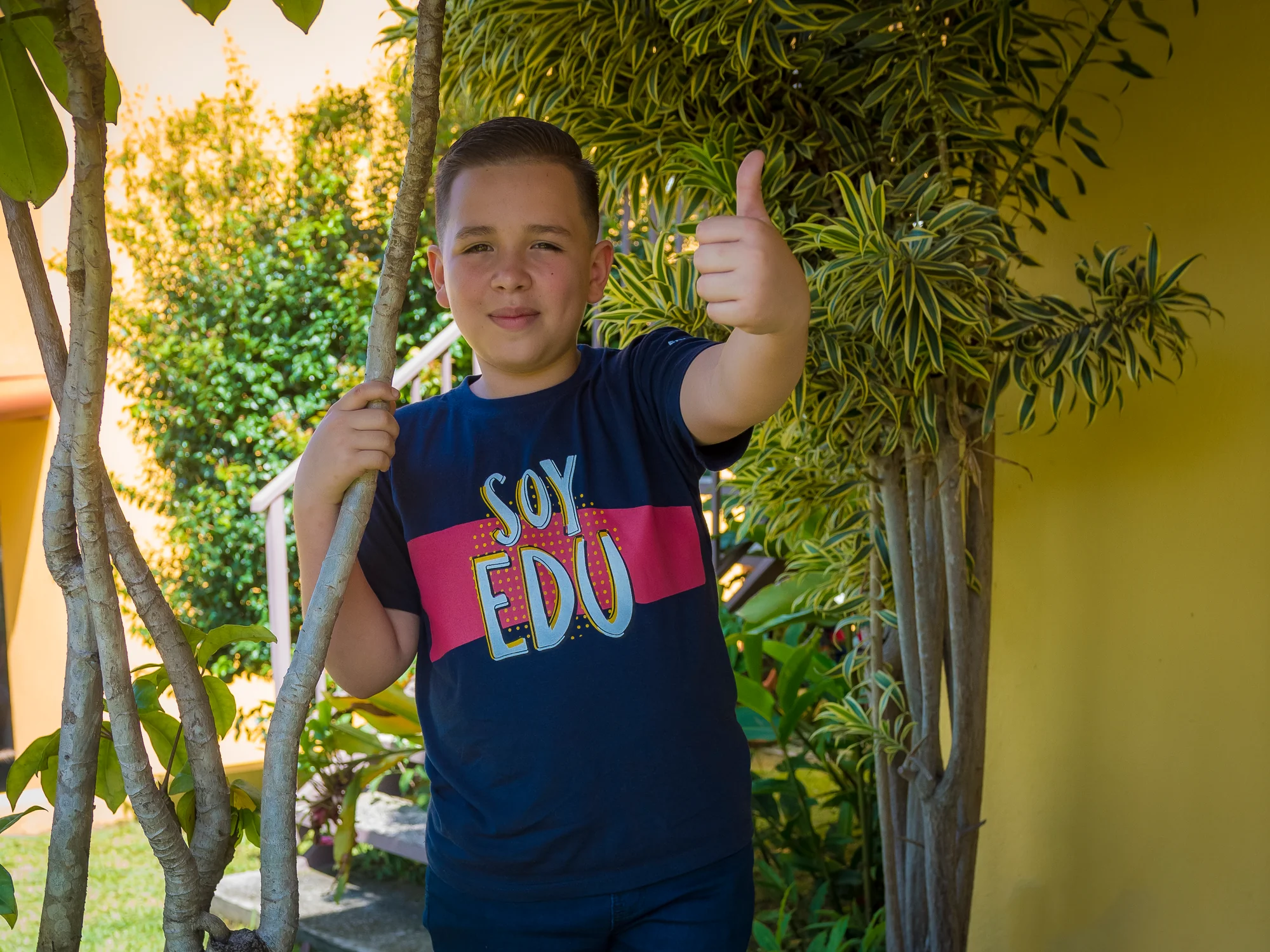 Beneficiario de Edunámica con la camiseta Soy Edunámica dando el pulgar arriba entre la vegetación de un jardín